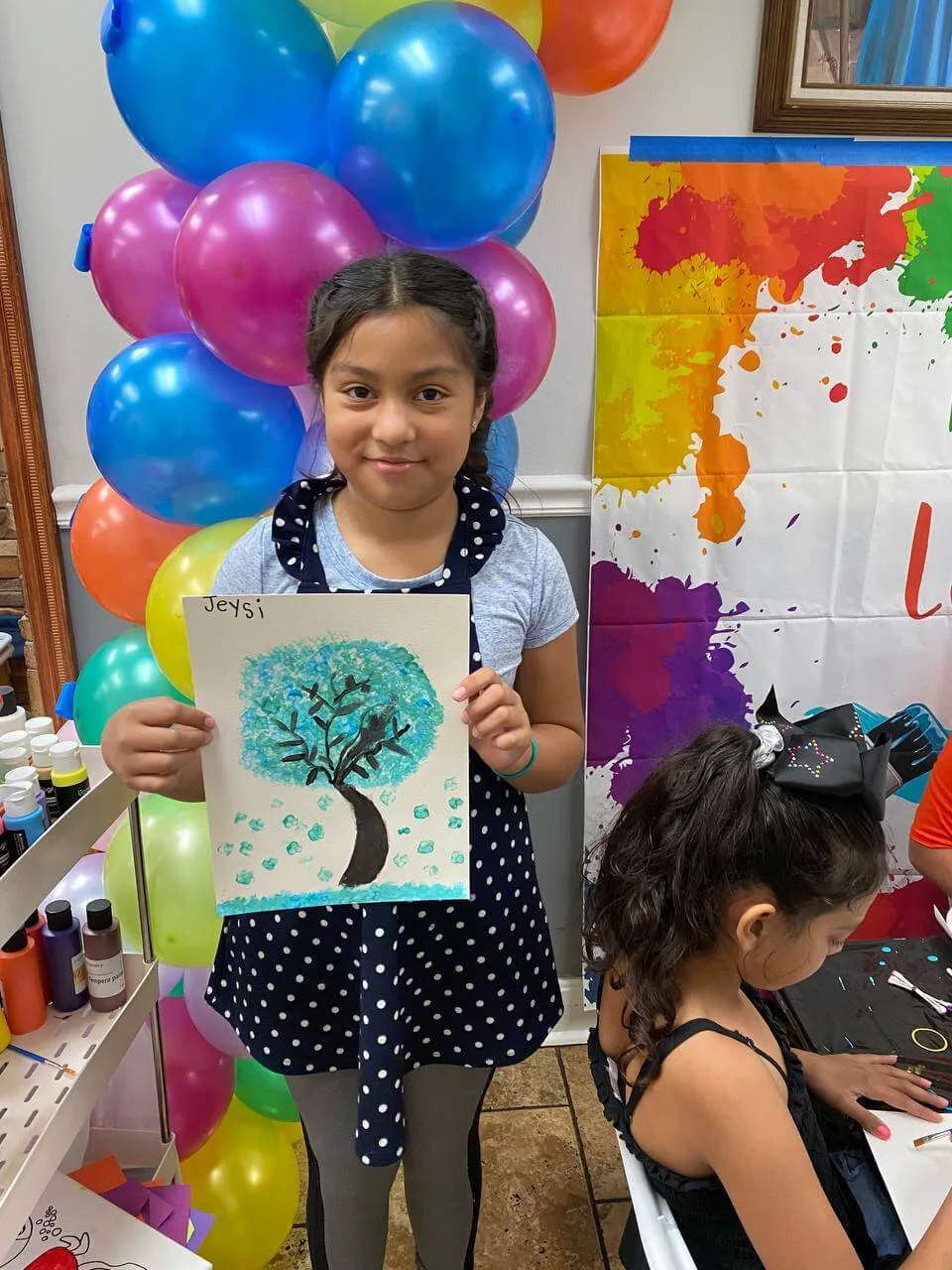 A smiling young artist holding a blue tree painting.
