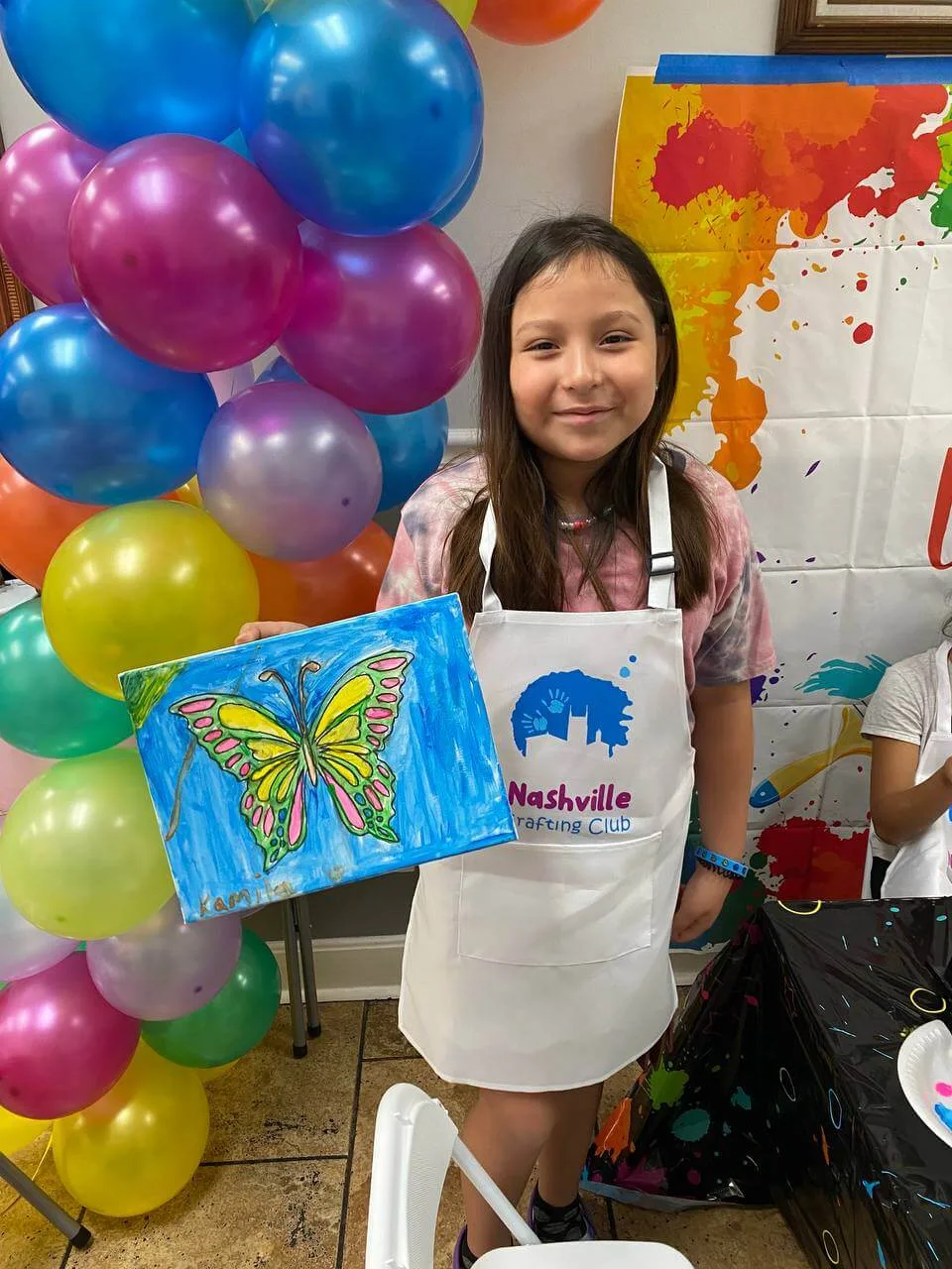 A child proudly displaying a butterfly painting at a craft party.