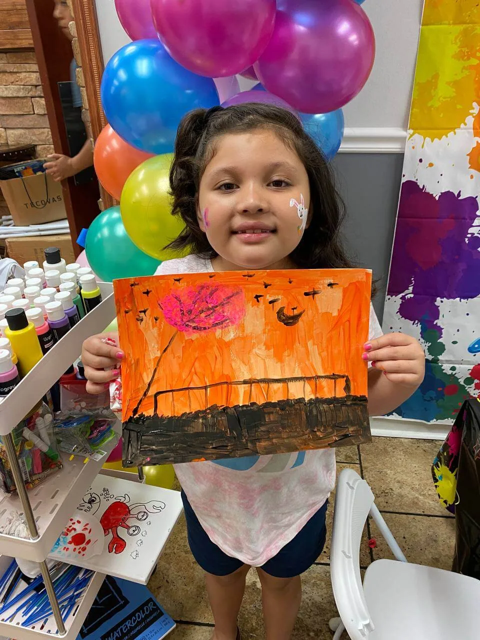 A young artist with an orange landscape painting at a craft party.