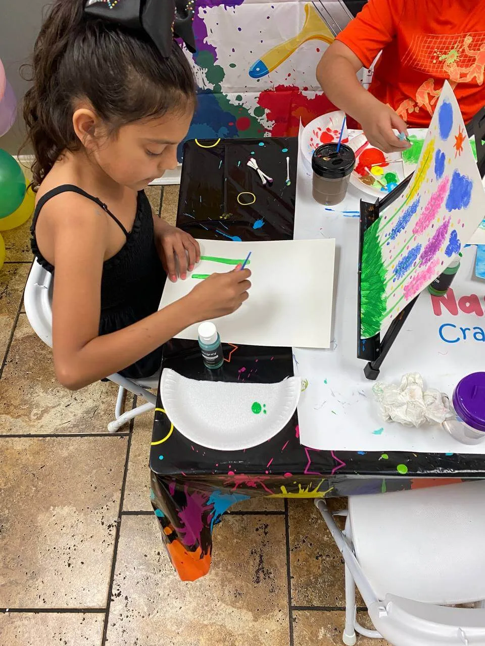 A child concentrating on painting a canvas at a craft party table.