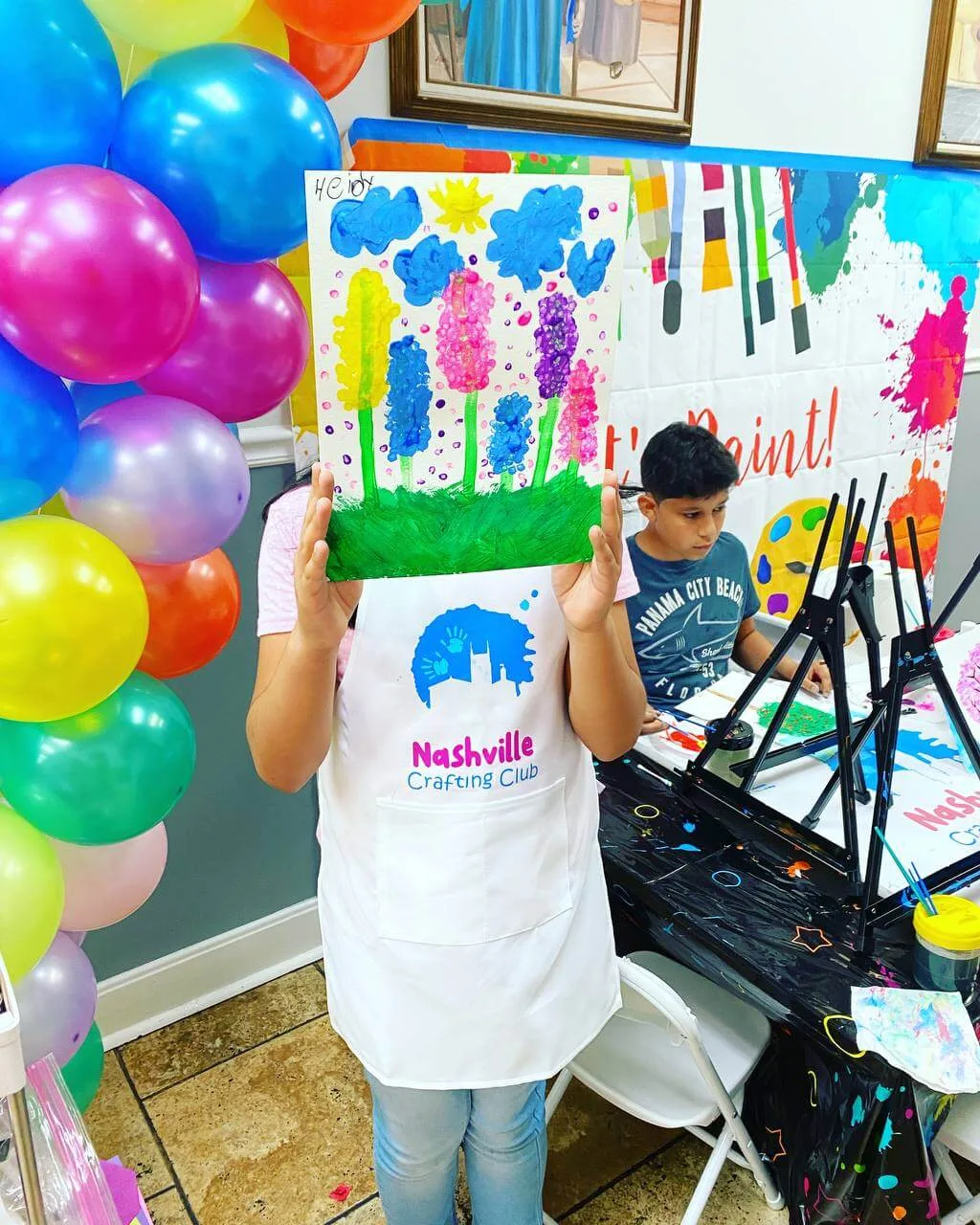 A young maker holding a colorful flower painting at a Nashville Crafting Club party.