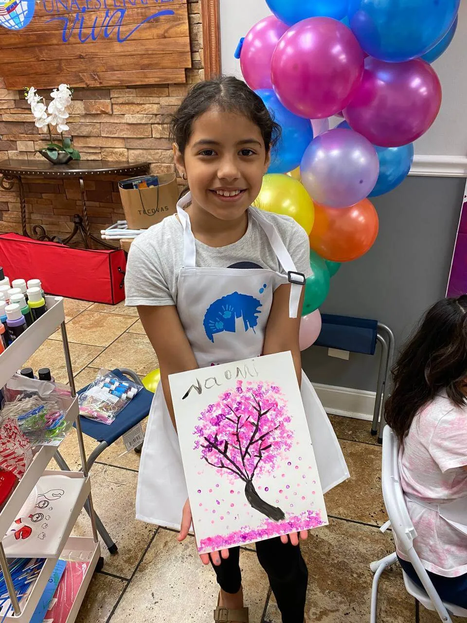 A smiling maker holding a pink tree painting.