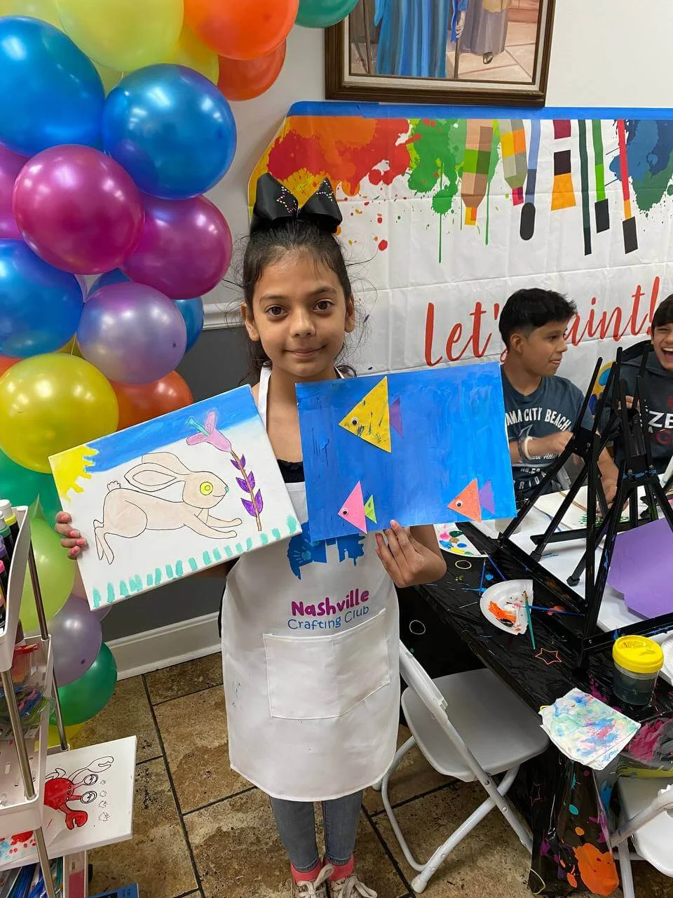 A child holding two handmade paintings with a rabbit and a fish.