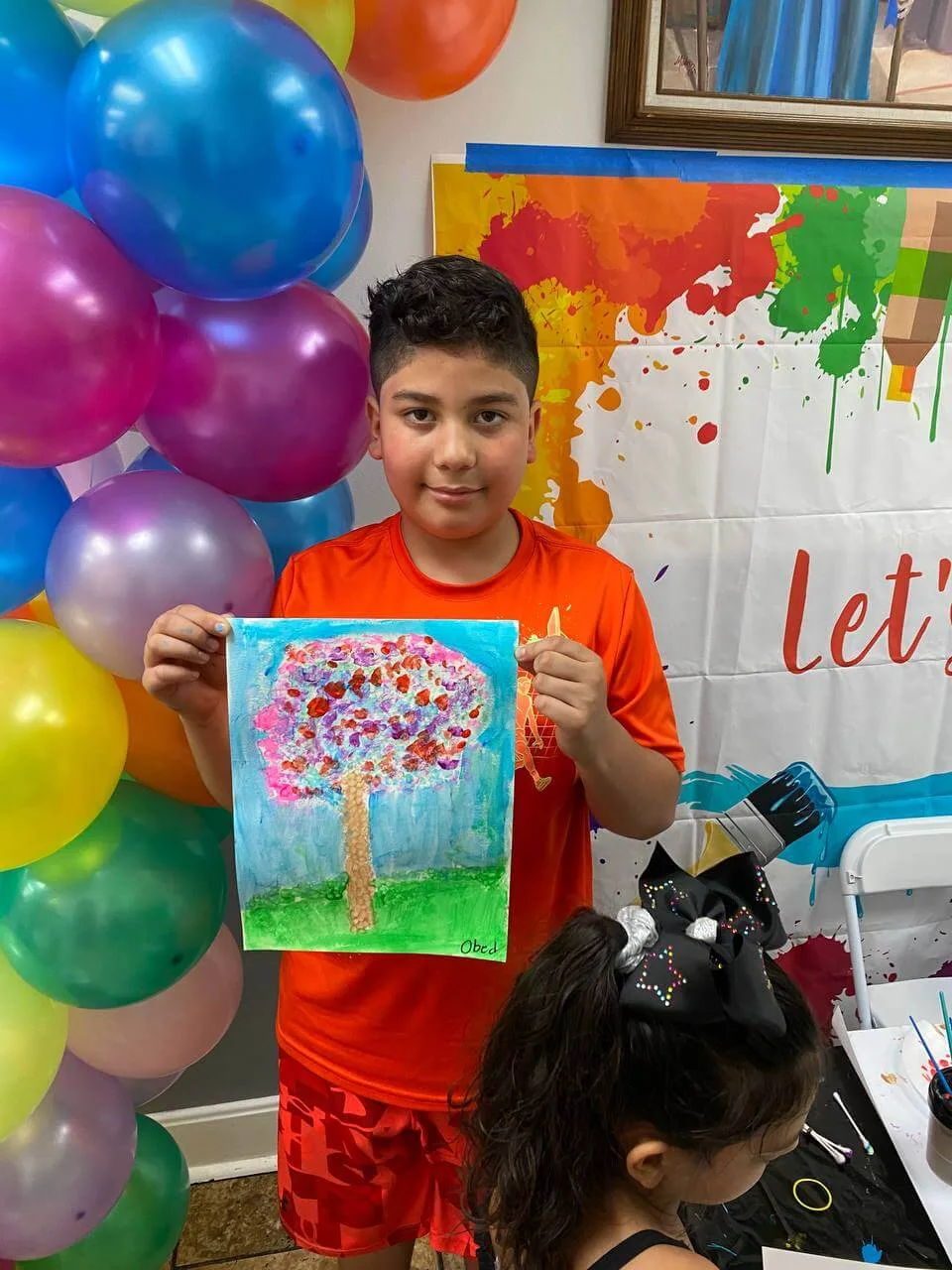 A young artist holding up a colorful tree painting at a birthday party.